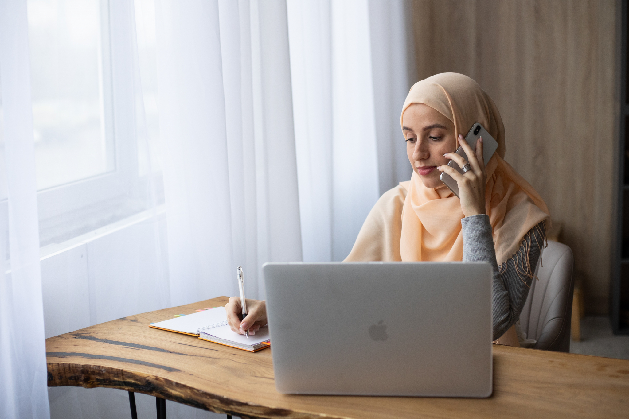 Woman in hijab on phone and facing a laptop